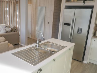 A kitchen island with a double sink and a tall silver refrigerator in the background at No 27 The Crab Pot Runswick Bay near Staithes