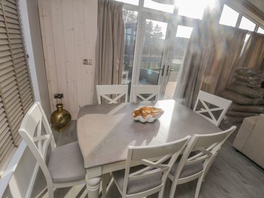 A dining table with six chairs and a decorative bowl near glass doors with curtains at No 27 The Crab Pot Runswick Bay near Staithes