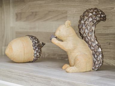 A wooden squirrel figurine holding an acorn next to a large wooden acorn on a wooden surface
