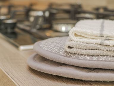 A close up of folded kitchen towels and pot holders on a wooden countertop near a gas stove