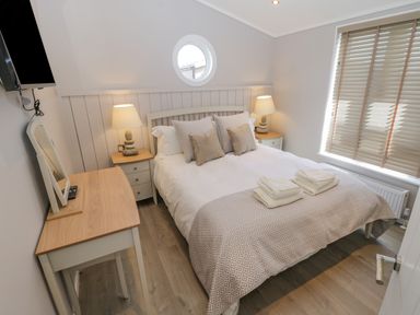 A bedroom with a double bed bedside tables lamps a window with blinds and a dressing table at No 27 The Crab Pot Runswick Bay near Staithes