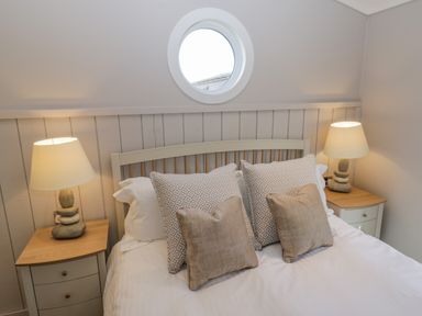 A bedroom with a bed flanked by two bedside tables each with a lamp and a round window above the headboard at No 27 The Crab Pot in Runswick Bay near Staithes
