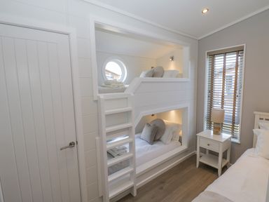 A bedroom with bunk beds a nightstand and a window with blinds at No 27 The Crab Pot in Runswick Bay near Staithes