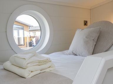 A bedroom with a circular window a pillow and folded towels on the bed at No 27 The Crab Pot Runswick Bay near Staithes