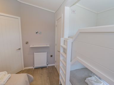 A room with a white bunk bed two closed white doors a radiator and a small wall shelf at No 27 The Crab Pot in Runswick Bay near Staithes