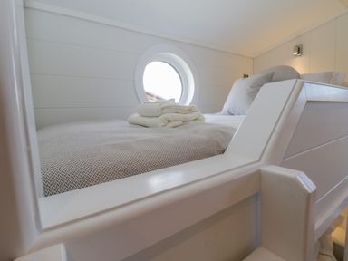A single bed with folded towels and a round window in a white bedroom at No 27 The Crab Pot Runswick Bay near Staithes