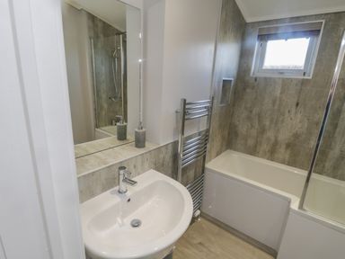 A bathroom with a sink countertop mirror radiator window and bathtub with shower at No 27 The Crab Pot Runswick Bay near Staithes