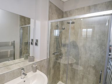 A bathroom with a sink, faucet, soap dispenser, large mirror, glass shower enclosure, and wall-mounted showerheads at No 27 The Crab Pot Runswick Bay near Staithes