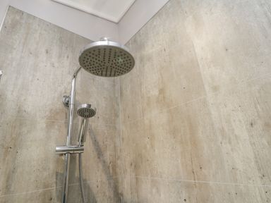 A shower area with a rainfall showerhead and handheld shower on a tiled wall at No 27 The Crab Pot Runswick Bay near Staithes