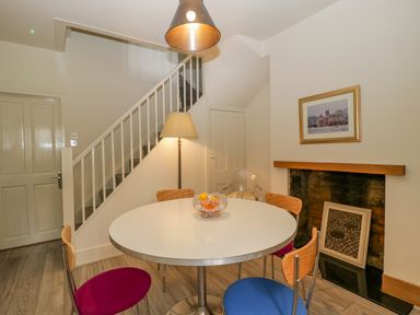A dining area with a round table and colorful chairs next to a staircase and a fireplace at Primrose Cottage in Winchcombe