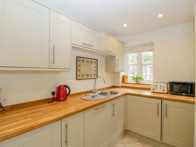 A kitchen with wooden countertops cupboards a red kettle a toaster a microwave and a window at Primrose Cottage in Winchcombe