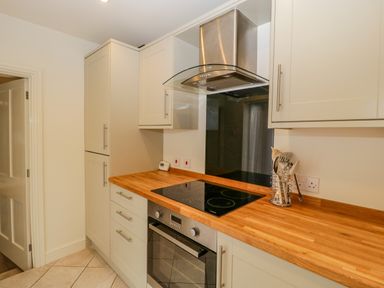 A kitchen with wooden countertops white cabinets an electric stove an oven and cooking utensils at Primrose Cottage in Winchcombe