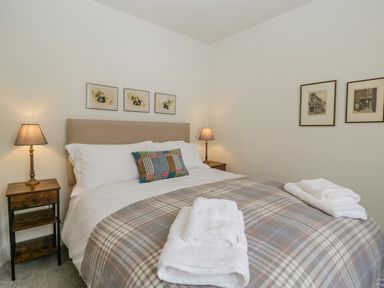A bedroom with a double bed two bedside tables with lamps and framed pictures on the walls at Primrose Cottage in Winchcombe