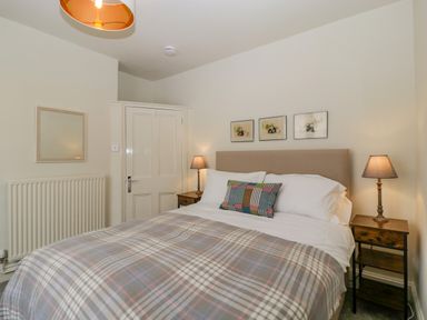 A bedroom with a double bed two lamps on bedside tables and three pictures above the bed at Primrose Cottage in Winchcombe
