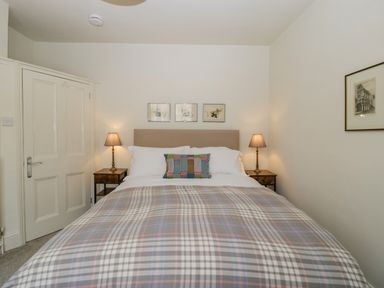 A bedroom with a double bed two bedside tables with lamps and framed pictures on the wall at Primrose Cottage in Winchcombe