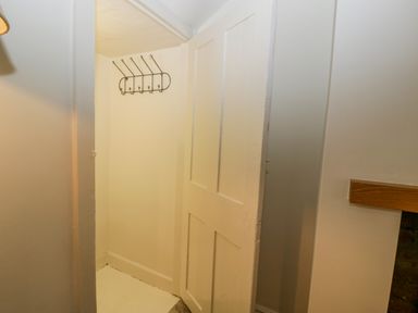 A small closet space with a wall-mounted coat rack and a partially open door at Primrose Cottage in Winchcombe