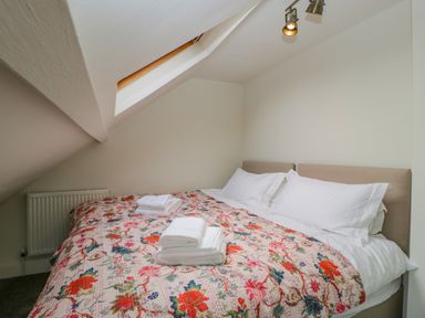 A bedroom with a double bed white pillows folded towels and a floral blanket at Primrose Cottage in Winchcombe