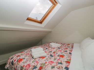 A bedroom with a slanted ceiling skylight window and a bed with a floral quilt and folded towels on top at Primrose Cottage in Winchcombe
