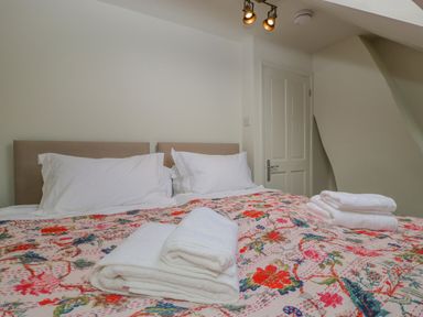 A bed with white pillows and floral bedspread with folded towels in a bedroom at Primrose Cottage Winchcombe