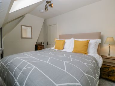 A bedroom with a bed with yellow pillows and gray patterned blanket at Primrose Cottage in Winchcombe
