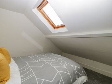 A bedroom with a bed covered with a gray patterned blanket under a skylight window at Primrose Cottage in Winchcombe