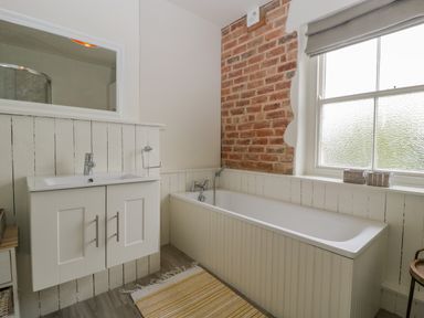 A bathroom with a sink cabinet bathtub exposed brick wall and a window at Primrose Cottage in Winchcombe