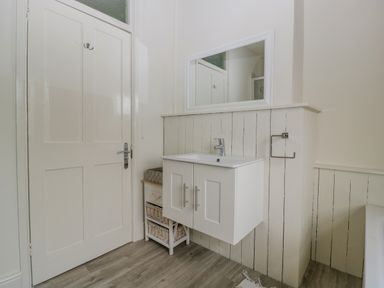 A bathroom with a white cabinet sink mirror wooden door and storage baskets at Primrose Cottage in Winchcombe