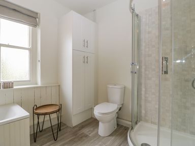 A bathroom with a toilet a shower a cabinet a wooden tray table and a window at Primrose Cottage in Winchcombe