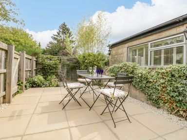 An outdoor patio with a table and four chairs next to a stone building with windows at Primrose Cottage in Winchcombe