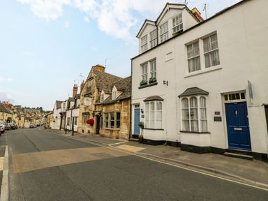 A street view with white cottages and a stone building on a road at Primrose Cottage in Winchcombe