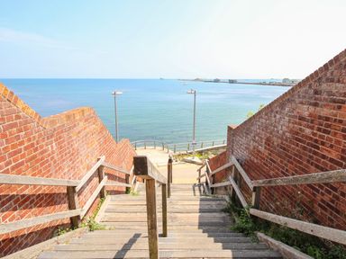 A wooden staircase with railings between brick walls leading down to a waterfront at Blanche Cottage Brewers Quay Harbour