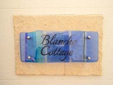 A blue glass sign with the text Blanche Cottage mounted on a stone slab on a wall at Blanche Cottage Brewers Quay Harbour