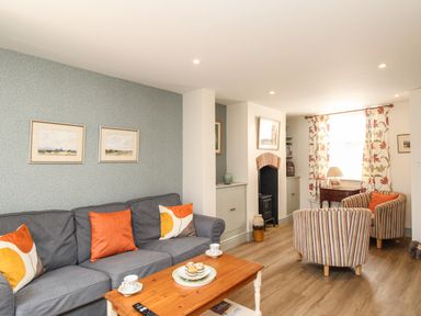 A living room with a gray sofa with orange and yellow cushions two striped armchairs a wooden coffee table and a fireplace at Blanche Cottage Brewers Quay Harbour