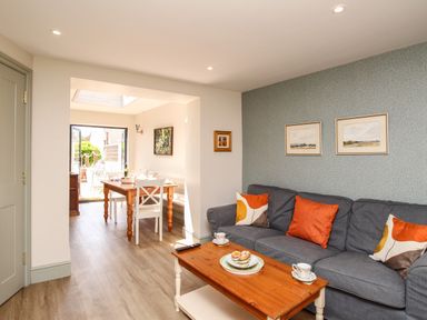 A living room with a gray sofa with colorful cushions and a wooden coffee table next to a dining area with a wooden table and white chairs at Blanche Cottage in Brewers Quay Harbour