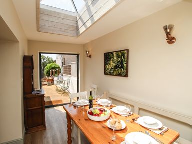 A dining area with a wooden table set with plates glasses fruit and bread with a skylight and open door to a patio at Blanche Cottage Brewers Quay Harbour