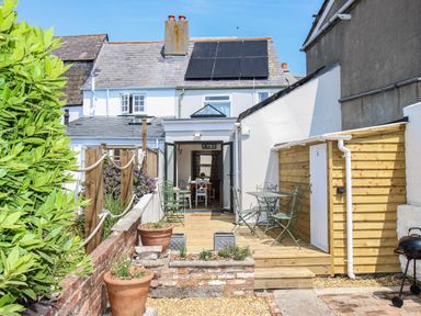 A patio with green metal chairs and tables outside a white house with solar panels at Blanche Cottage in Brewers Quay Harbour