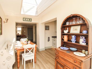 A dining area with a wooden dining table set for four and a wooden cabinet displaying glassware and ceramics at Blanche Cottage Brewers Quay Harbour