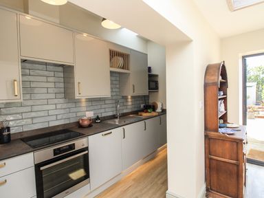 A kitchen with modern cabinets appliances and a wooden cupboard near a glass door at Blanche Cottage Brewers Quay Harbour