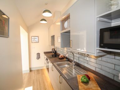 A narrow kitchen with cabinets a sink a stove a microwave and a chopping board with vegetables at Blanche Cottage in Brewers Quay Harbour