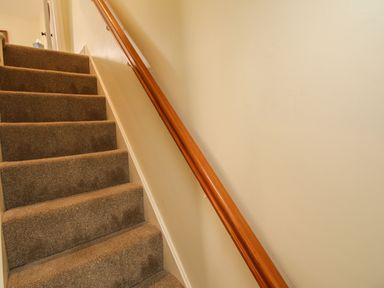A carpeted staircase with a wooden handrail and beige walls at Blanche Cottage in Brewers Quay Harbour