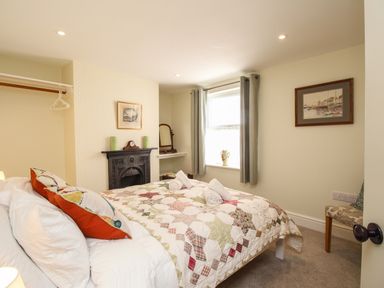 A bedroom with a bed covered by a quilt and pillows two rolled towels on the bed a small fireplace a window with curtains and framed pictures at Blanche Cottage Brewers Quay Harbour