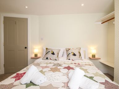 A bedroom with a double bed with patterned quilt and bird pillows bedside lamps and a beige door at Blanche Cottage Brewers Quay Harbour