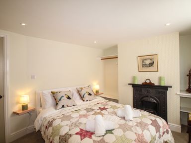 A bedroom with a bed with patterned quilt pillows and towels with lamps on wall shelves and a fireplace at Blanche Cottage Brewers Quay Harbour