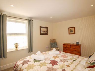 A bedroom with a bed covered with a patterned quilt two rolled towels on the bed a wooden chest of drawers a chair and two framed pictures on the walls at Blanche Cottage in Brewers Quay Harbour