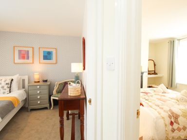 View of two bedrooms separated by a white wall one with a grey nightstand and framed pictures the other with a bed covered with a quilt at Blanche Cottage Brewers Quay Harbour