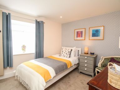 A bedroom with a single bed a bedside table lamp two framed pictures blue curtains and a chair at Blanche Cottage Brewers Quay Harbour