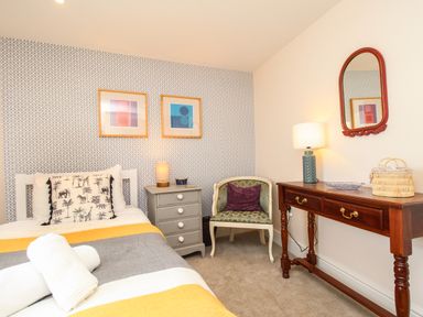 A bedroom with a bed yellow and gray blanket a gray nightstand a chair a wooden table with a lamp and mirror at Blanche Cottage Brewers Quay Harbour