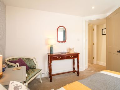 A bedroom with a wooden table with a lamp and mirror a green upholstered chair and an open door at Blanche Cottage in Brewers Quay Harbour