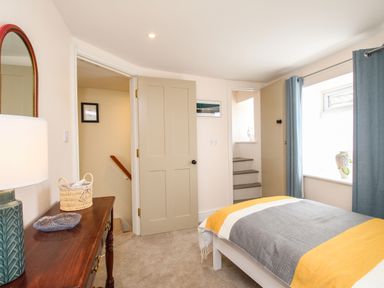 A bedroom with a single bed beside a window and a wooden dresser with a lamp and basket at Blanche Cottage Brewers Quay Harbour