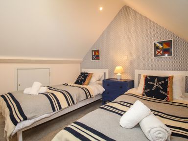 A bedroom with two single beds a blue nightstand with a lamp and patterned wallpaper at Blanche Cottage Brewers Quay Harbour